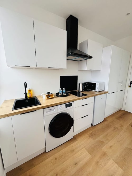Cuisine moderne blanche avec électroménagers noirs, plan de travail en bois et évier en acier inoxydable aux Logis d'Emma