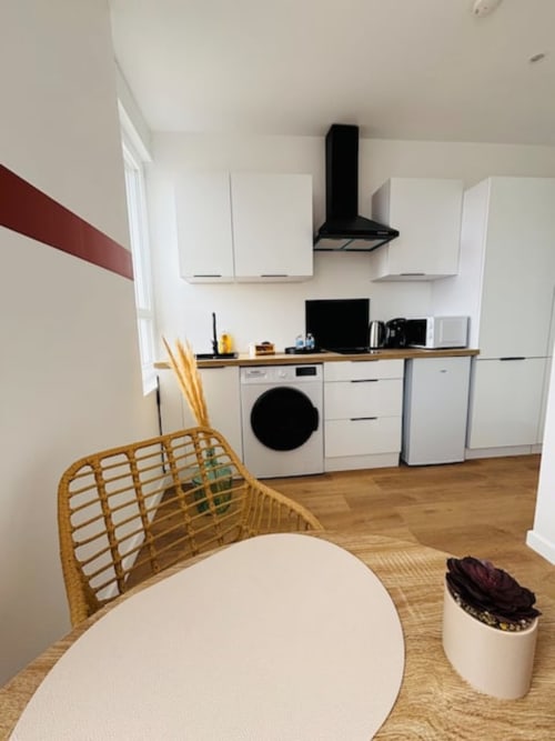 Cuisine moderne aux Logis d'Emma : meubles blancs, lave-linge et coin repas avec chaise tissée