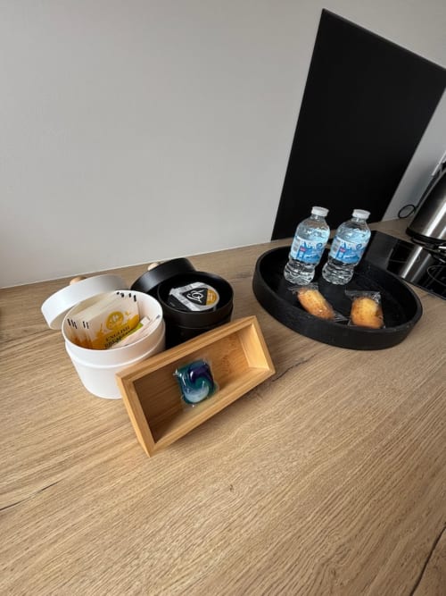 Plateau de bienvenue à l'hôtel avec bouteilles d'eau, viennoiseries et accessoires sur un bureau en bois aux Logis d'Emma