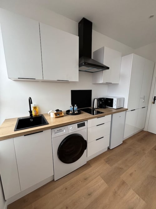 Kitchenette moderne de l'appartement The Yogi aux Logis d'Emma, avec armoires blanches, plan de travail en bois et électroménagers noirs