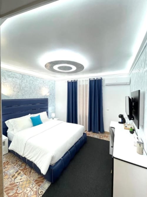 Moderno dormitorio del Hotel Boutique Galeon con cama azul marino, ropa de cama blanca, cortinas azules, luz LED en techo, TV y