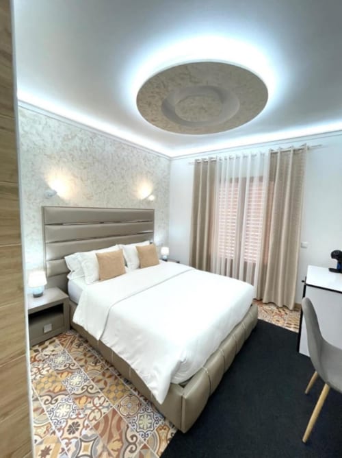 Moderno dormitorio doble en Hotel Boutique Galeon con lámpara LED de techo, cama tapizada beige y cortinas con vistas a la ciudad