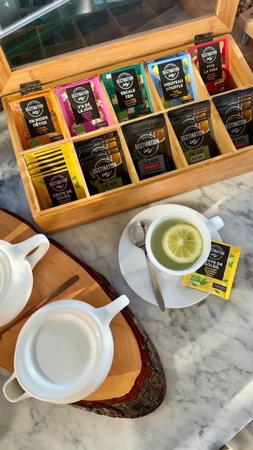 Collection de thés d'exception à l'Hôtel Reine D'Azur : tasses blanches, thé au citron et rangement bois sur table marbre.