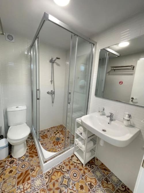 Baño moderno del Hotel Boutique Galeon con ducha de cristal, lavamanos blanco, inodoro y piso con azulejos estampados