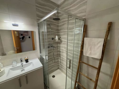 Banheiro moderno no Al Mare Ocean View em Albufeira com chuveiro em vidro, pia, espelho e escada de madeira para toalhas