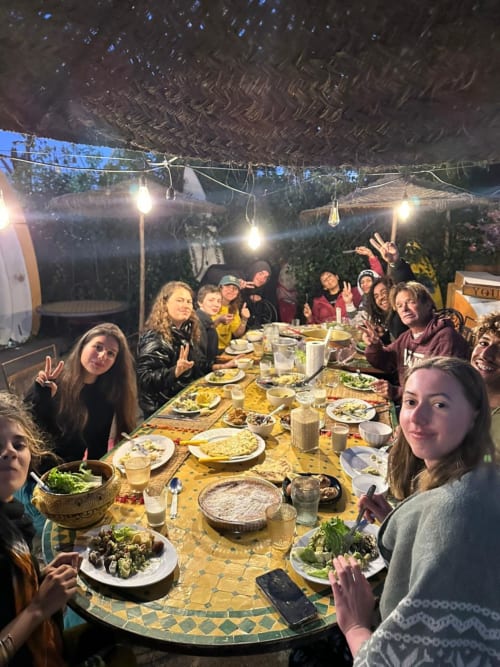 Cena grupal en el albergue Yousurf Surfhouse en Essaouira, Marruecos con huéspedes disfrutando de comidas bajo las luces nocturnas