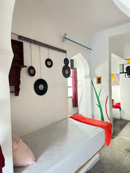 Bright female dorm room at Yousurf Surfhouse in Essaouira with vinyl record wall art, white bed, red accents, and decorative