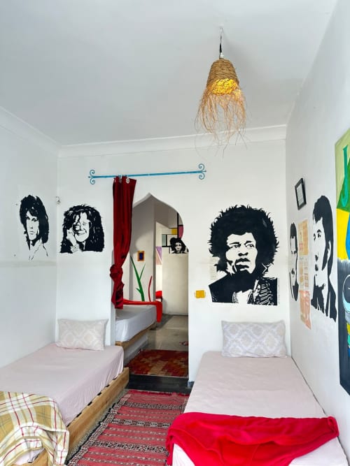 Female dorm room at Yousurf Surfhouse hostel in Essaouira with four beds, rock band posters, and shared bathroom
