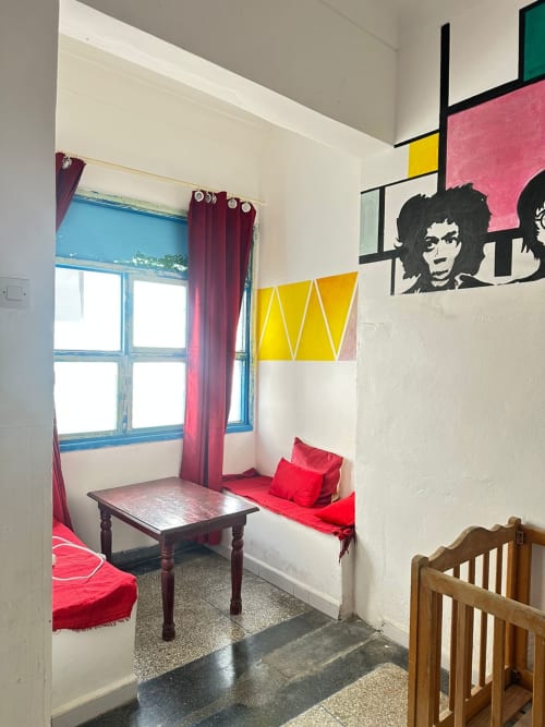 Yousurf Surfhouse dorm room in Essaouira with red bedding, colorful modern art, blue-framed window, and wooden crib
