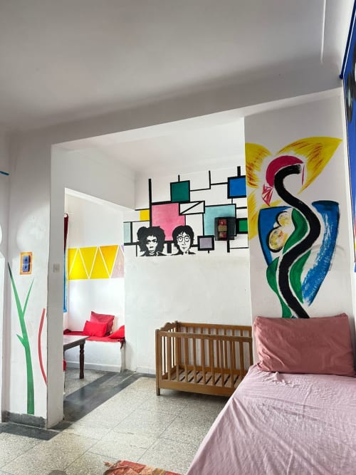 Colorful hostel dorm room at Yousurf Surfhouse in Essaouira with vibrant wall art, wooden crib, and pink bedding