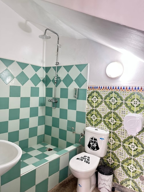 Shared bathroom in Yousurf Surfhouse hostel with teal and white checkered tiles, rainfall showerhead, and Star Wars themed