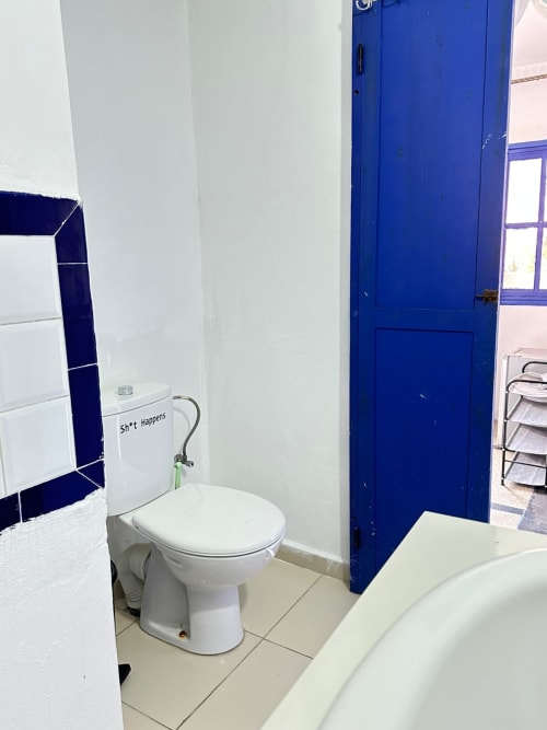 Bathroom in Berber room at Yousurf Surfhouse hostel, Essaouira, with white toilet, blue door and tiled walls