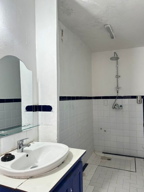 Berber room bathroom at Yousurf Surfhouse hostel in Essaouira with white tiles, dark blue accent stripe, sink, mirror, and