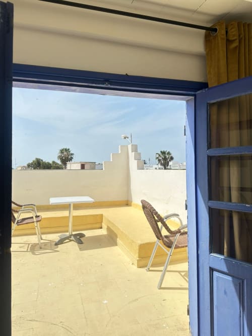 Blue door opening to yellow terrasse with chairs, table and city view at Yousurf Surfhouse, Essaouira