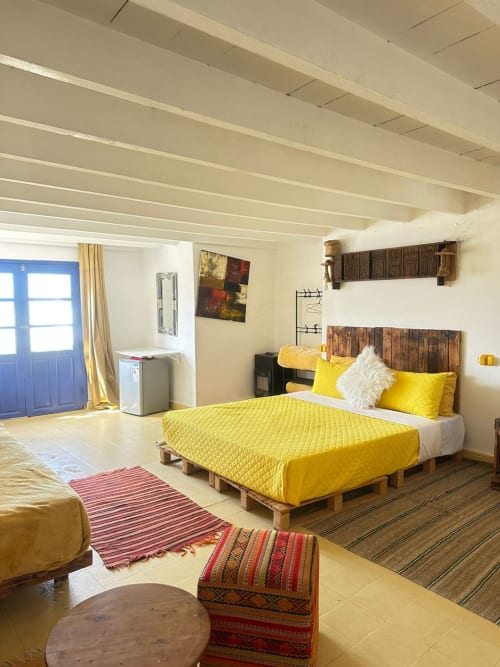 Sahara room at Yousurf Surfhouse hostel in Essaouira with yellow bedding, wooden pallet bed, and city views through blue door