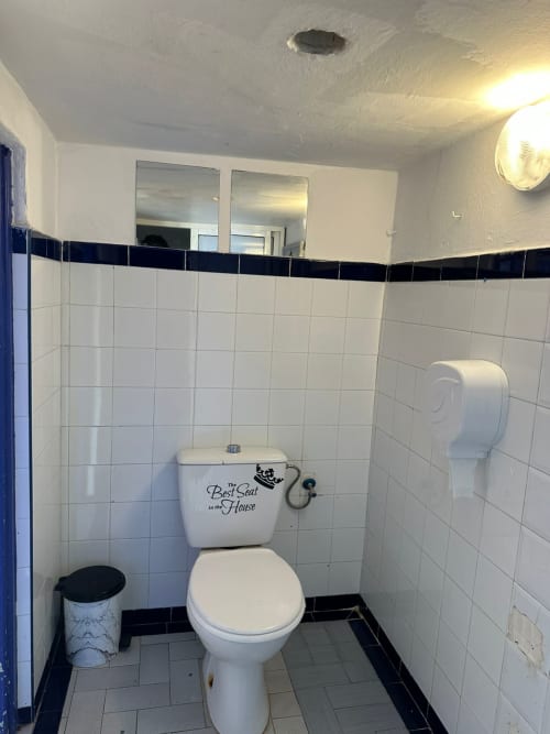 Clean shared bathroom toilet at Yousurf Surfhouse hostel in Essaouira with white tiles and decorative seat cover