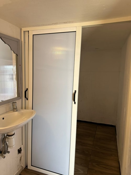 Shared bathroom with sink and frosted glass shower door at Yousurf Surfhouse hostel, Essaouira