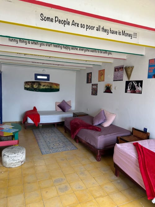 Three-bed male dorm room at Yousurf Surfhouse hostel in Essaouira with colorful bedding, shared bathroom, and inspirational