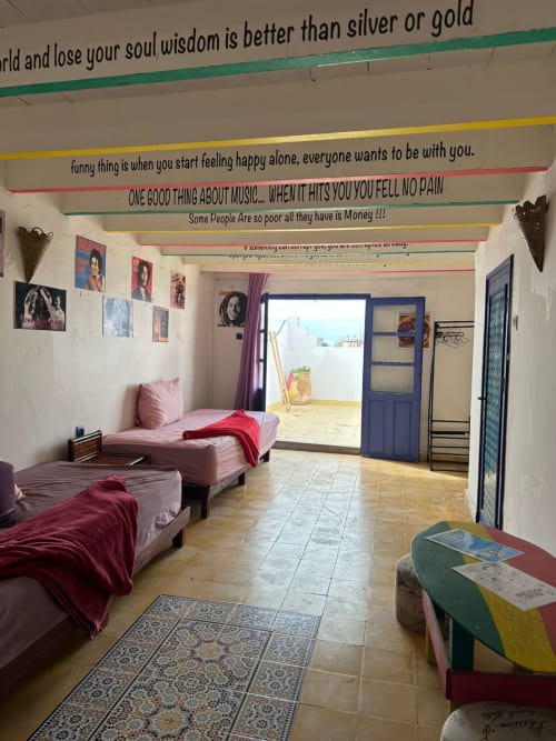 Yousurf Surfhouse dorm room in Essaouira with three beds, colorful ceiling beams, and motivational wall quotes.