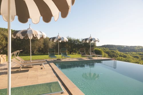 La piscina a sfioro dell'Agriturismo Il Serraglio con ombrelloni a righe, lettini e vista sulla campagna toscana vicino a Montepulciano