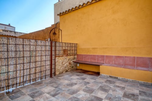 Terraza del hotel Finques Garcia Enrich en Palafrugell con paredes amarillas, banco rojo y puerta rústica de metal