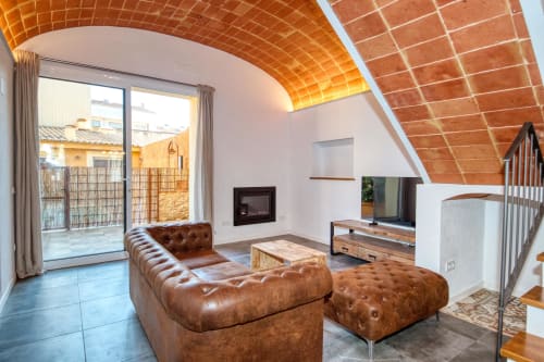 Salón moderno estilo loft en Finques Garcia Enrich, Palafrugell con techo de ladrillo terracota, sofá de cuero y chimenea