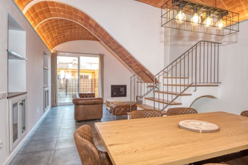 Comedor tipo loft moderno en Palafrugell con mesa de madera, sillas de cuero, techo abovedado de ladrillo y escalera metálica