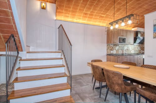 Comedor moderno con escalera de madera, cocina y sillas de cuero marrón en Finques Garcia Enrich, Palafrugell