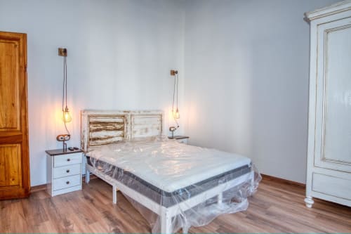 Dormitorio luminoso en Finques Garcia Enrich en Palafrugell con cama de madera, mesilla blanca, lámparas colgantes y suelo de madera