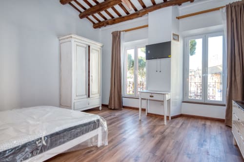 Dormitorio espacioso en Finques Garcia Enrich, Palafrugell con vigas de madera vista, armario, escritorio y vistas al balcón.