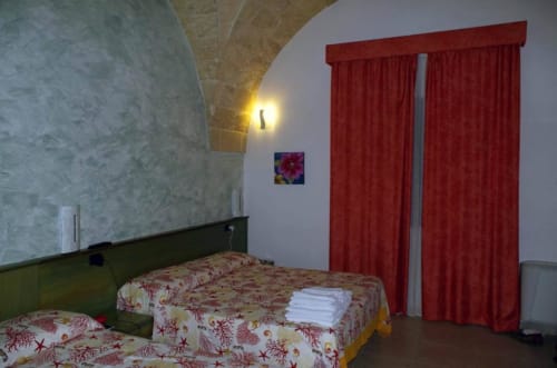 Camera tripla a B&B Villa Arneide a Torre Lapillo con letti gemelli, tende rosse e soffitto ad arco
