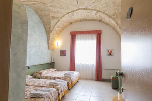 Camera tripla di B&B Villa Arneide a Torre Lapillo con tre letti, soffitto ad arco e finestra con tende rosse