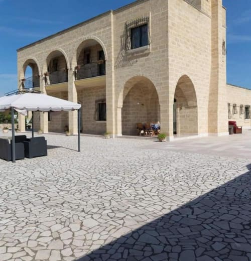 Cortile di B&B Villa Arneide a Torre Lapillo con archi in pietra, ombrelloni bianchi e pavimentazione decorativa