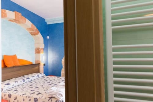 Camera luminosa della B&B Villa Arneide a Torre Lapillo con pareti blu, letto in legno, cuscini arancioni e biancheria a tema marino