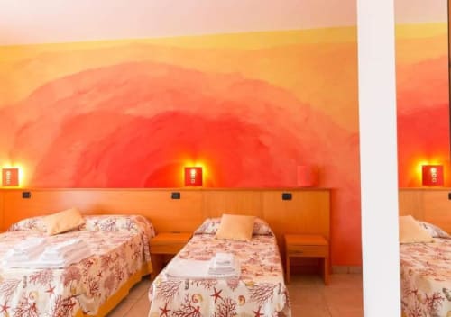 Camera quadrupla luminosa al B&B Villa Arneide di Torre Lapillo con letti gemelli, biancheria a motivi corallini e bagliore arancione