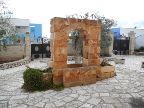 Antico pozzo in pietra nella corte della B&B Villa Arneide, Torre Lapillo Italia, con cancellate blu e piazza pavimentata