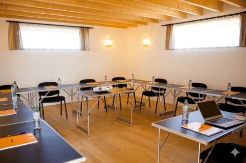 Salle de conférence moderne à l'Espace Ker Gana avec poutres en bois, tables disposées, chaises et carafes d'eau à Plourin