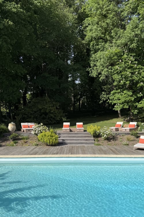 Luxury pool area at La Maison 1680 with turquoise water, wooden deck, orange loungers, and mature trees in Couches, France