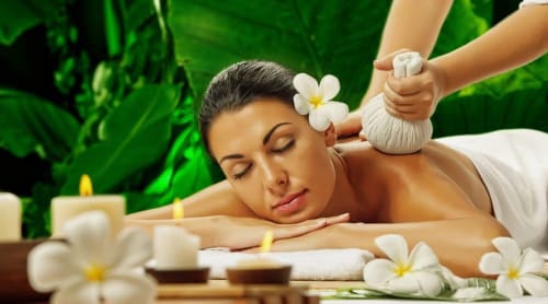 Femme se relaxant lors d'un massage bien-être entouré de fleurs blanches au centre Yousurf Surfhouse à Essaouira