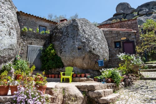 Charming stone courtyard at Moinho do Maneio guesthouse in Penamacor, featuring rustic buildings, massive boulders, green