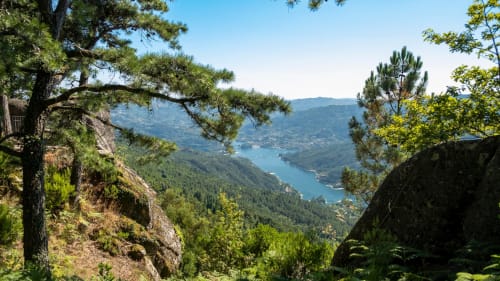 Vista panorâmica do vale montanhoso com lago turquesa, encostas florestadas e estruturas de pedra na Quinta da Coutada, Arcos de