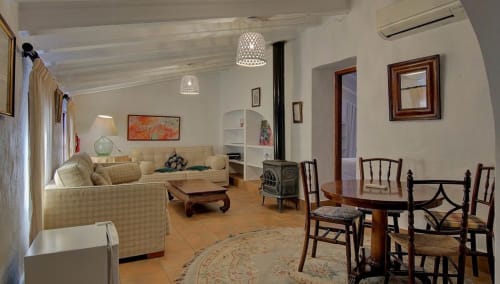 Bright living room at Casa Gallinera's Els Llombos with cream sofa, dining table, stove, and mountain views in Benissivà