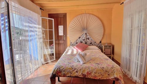 Dormitorio acogedor en Casa Gallinera en Benissivà con ropa de cama floral, cabecero ventilador decorativo y paredes naranja cálidas