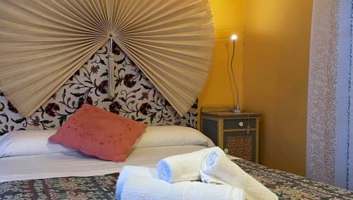 Cozy bedroom at Casa Gallinera in Benissivà with decorative headboard, coral pillow, and yellow accent wall