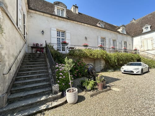 Charmante cour du gîte Domaine Pont Juillet à Fontaines avec façade en pierre, plantes fleuries et voiture de sport blanche