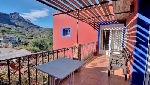 Balcony at Casa Gallinera in Benissivà with mountain views, table, chair, and red building with pergola