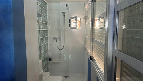 Modern glass shower enclosure in Casa Gallinera vacation home room with glass block wall and mountain view window, Benissivà