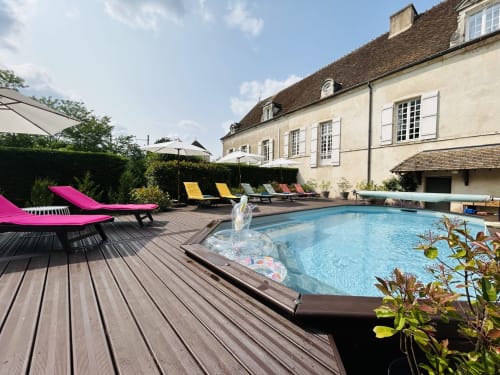 Espace piscine du Domaine Pont Juillet avec transats roses, terrasse en bois et maison en pierre à Fontaines