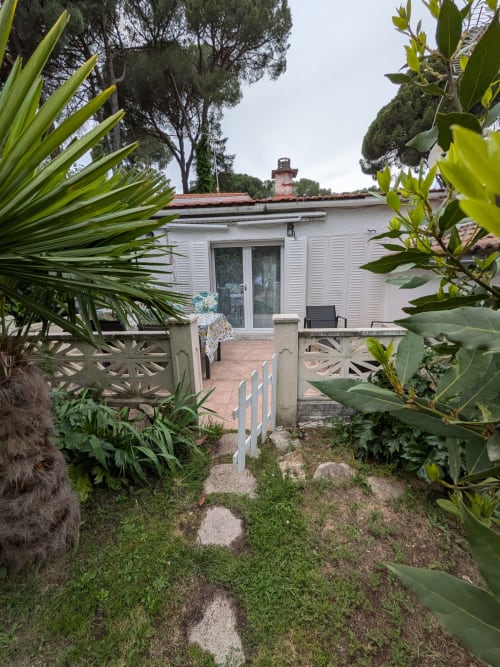 Entrada de cabaña blanca con portón, plantas tropicales y vista al lago en Las Casitas de Noe, Layos