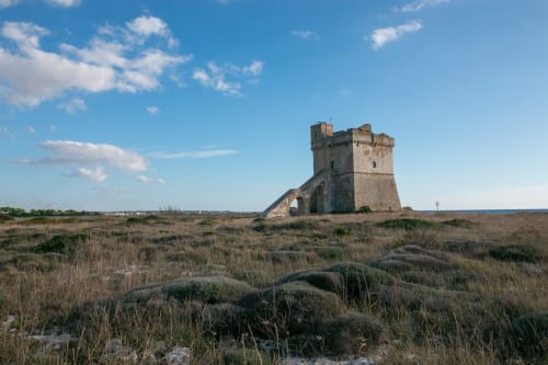Torre storica in pietra a Torre Lapillo, Italia, circondata da vegetazione costiera e cielo azzurro